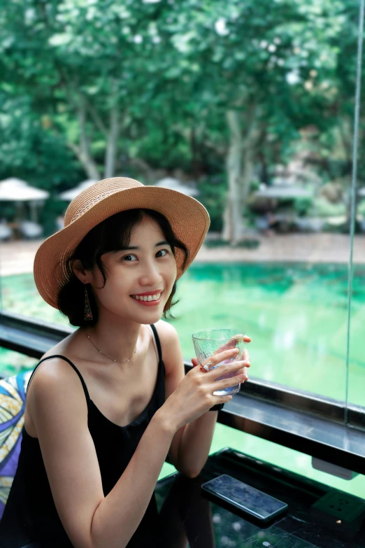 a beautiful young lady in a hat and black tank top holding a beverage