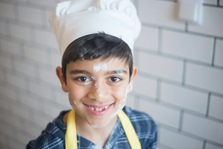 a boy with an apron and a hat on is smiling