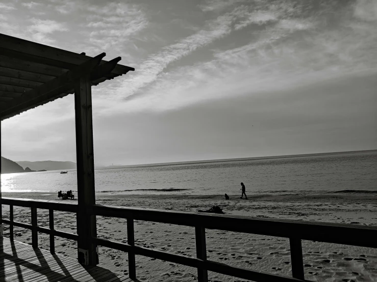 black and white pograph of a person walking on a beach near an ocean