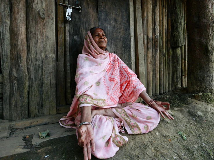 an old woman sitting on the ground near a wooden wall