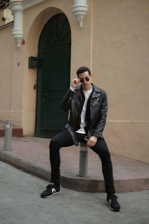 a man sits on a pole in front of a building while talking on his cell phone