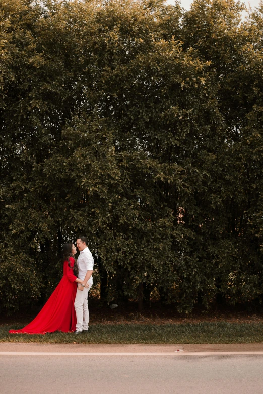 a man and woman in red cloaks are standing by a green tree