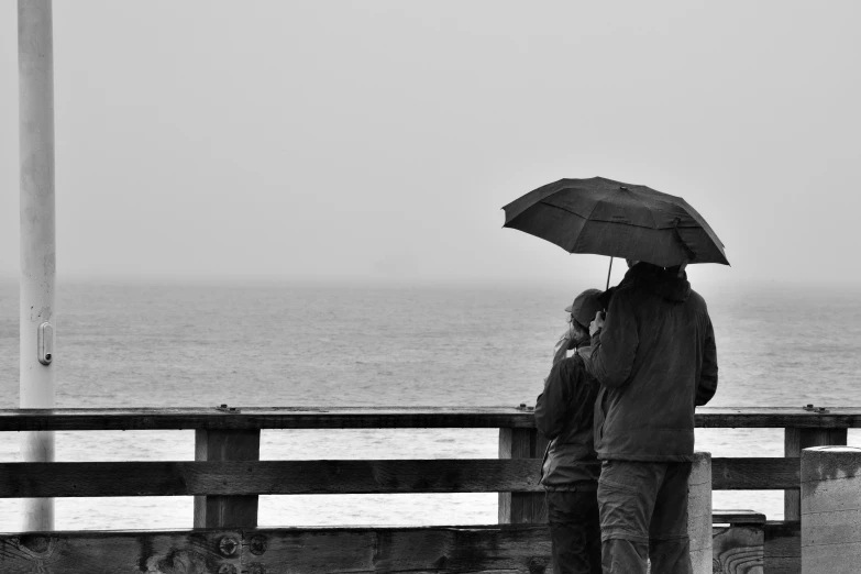 black and white pograph of a couple under an umbrella looking at the ocean