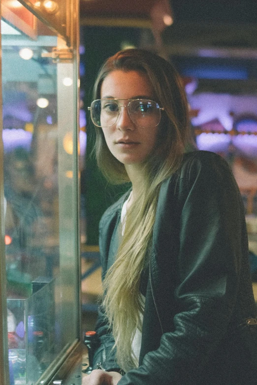 a woman with glasses and a black jacket staring out the window