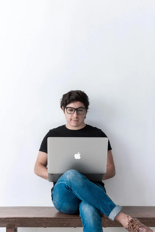 a man with glasses on sitting on top of a wooden bench with a laptop