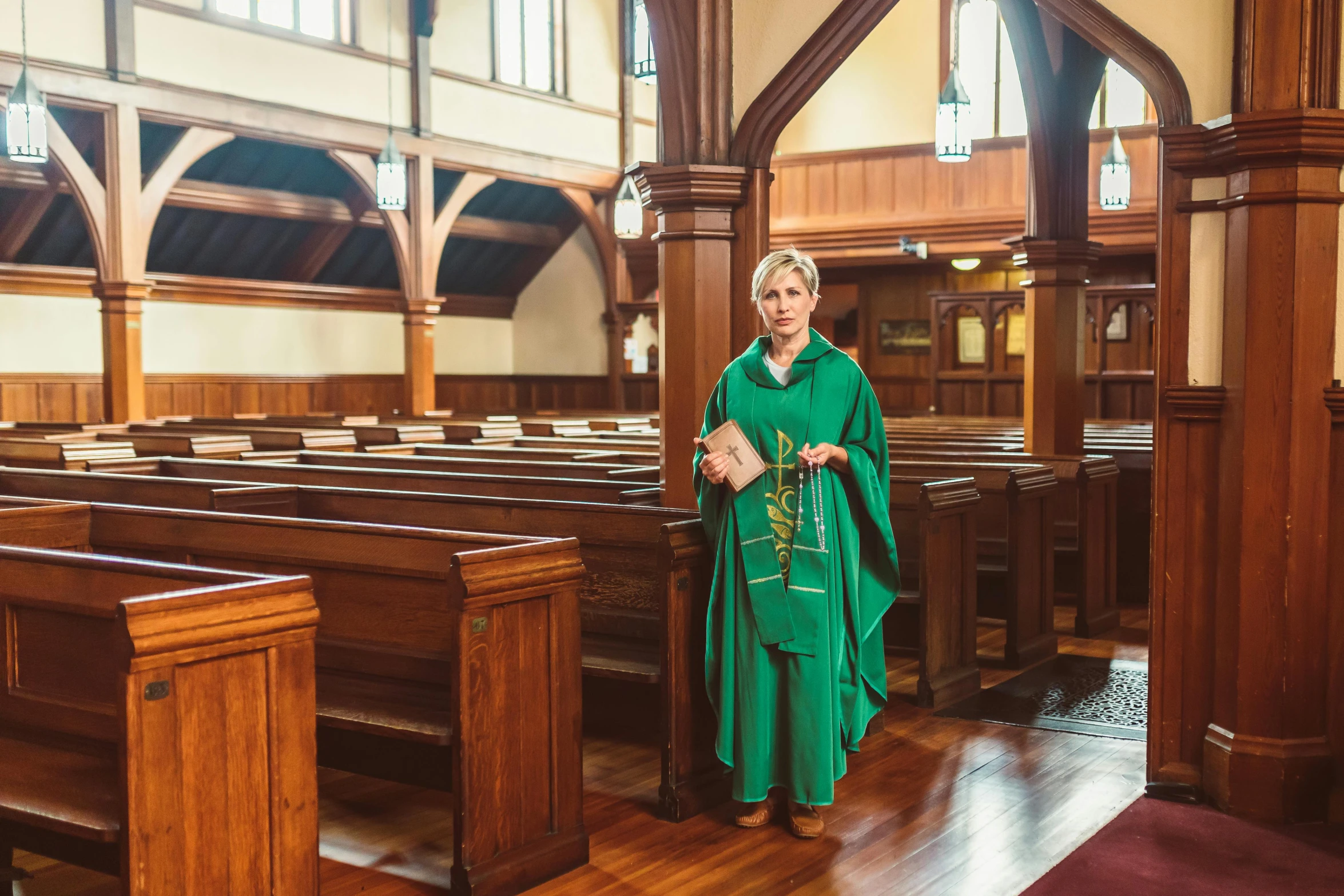 an older lady wearing a green cloak is standing in the middle of pews