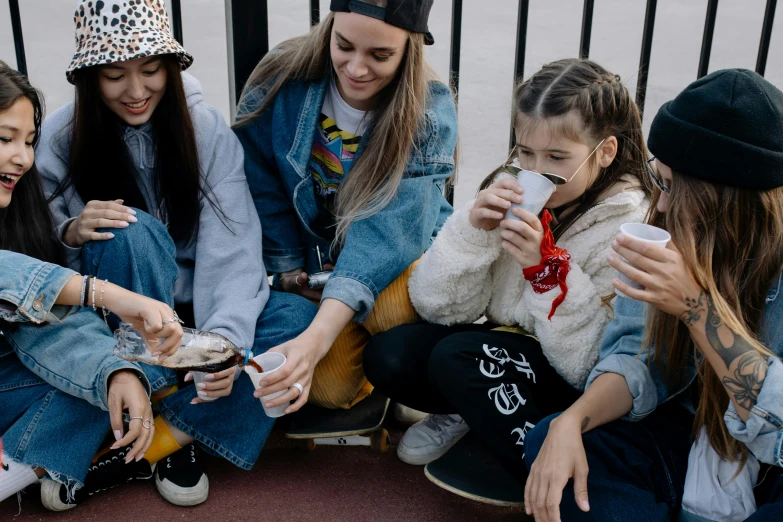 group of girls sitting on a sidewalk looking at a cellphone