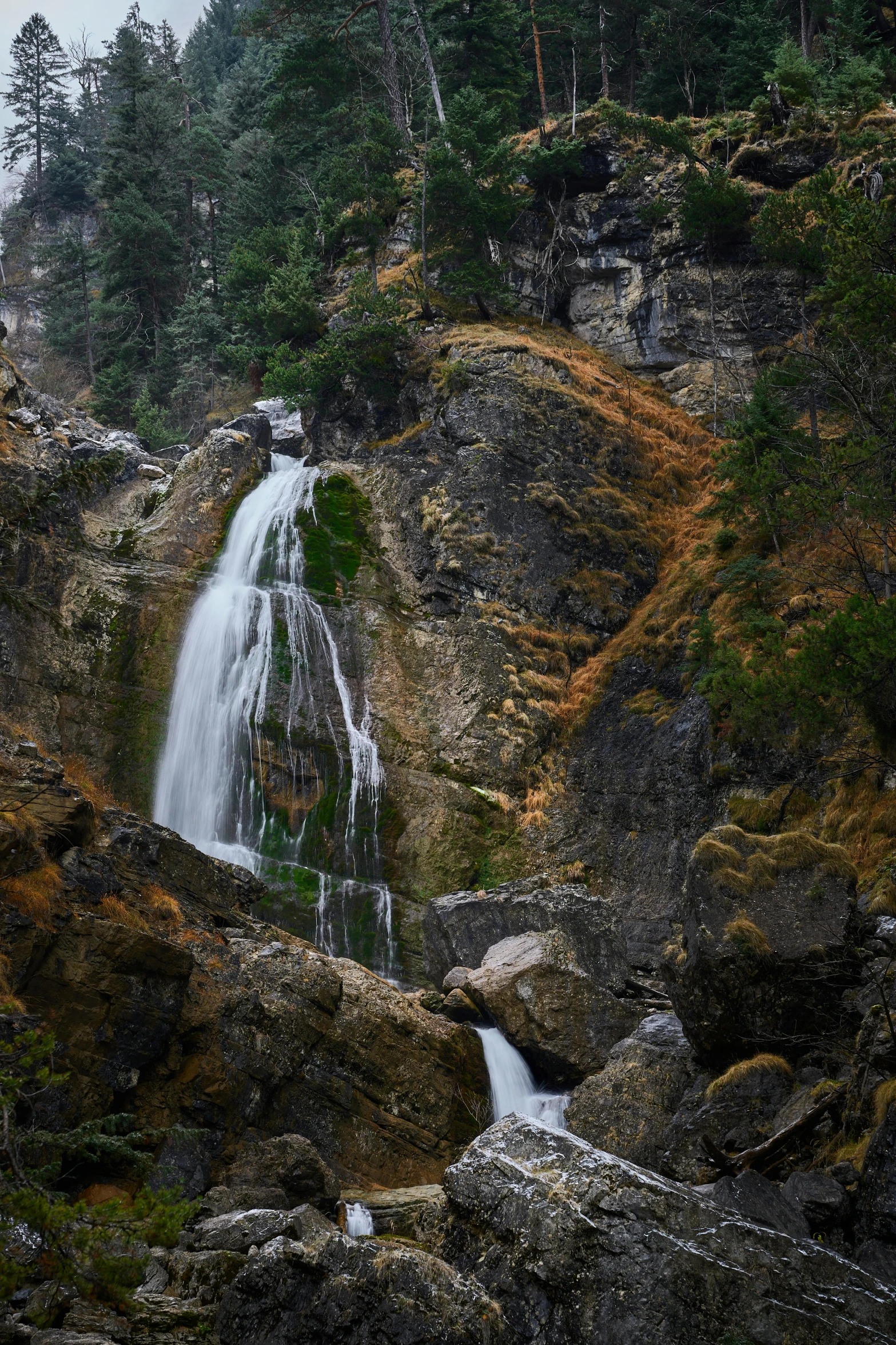 a waterfall running into a small creek in a mountain