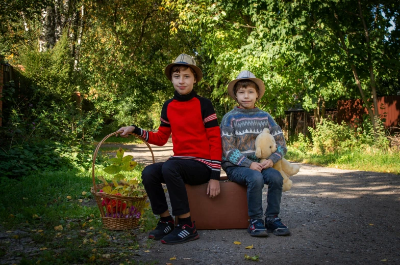 two boys sitting on top of suitcases on a road