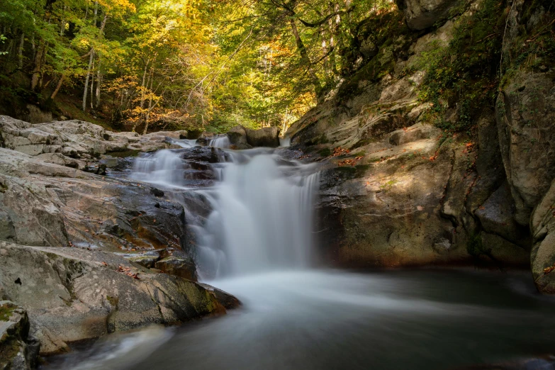 small waterfall cascading from two huge rocks into a river