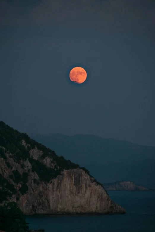 a large orange moon in the sky above water