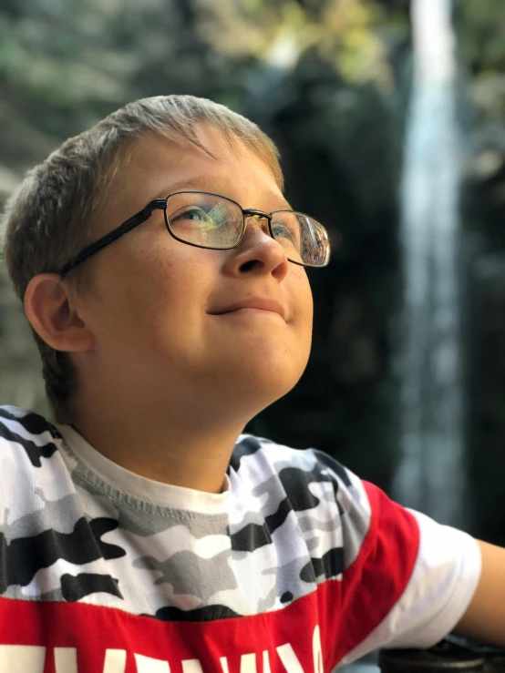 a boy wearing glasses looking up at the water fall