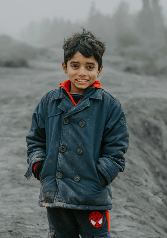 a  in a peacoat smiling while standing on a sandy beach