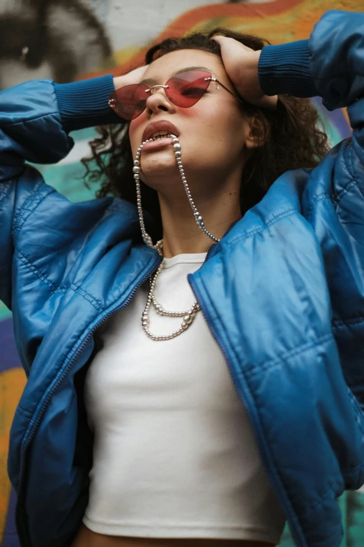 a young woman wearing sun glasses, a white shirt and blue coat is posing for a picture with her hands on her head