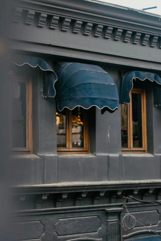 a grey building with two windows and blue awnings