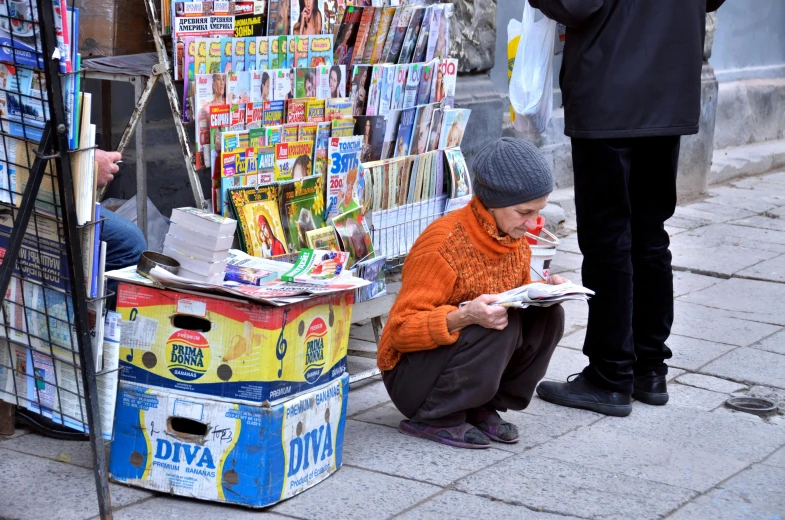 people are sitting down reading newspapers while one person stands near