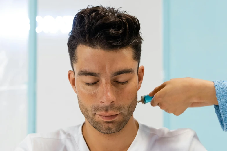 a man with a brush on his ear looks down as he shaves his head