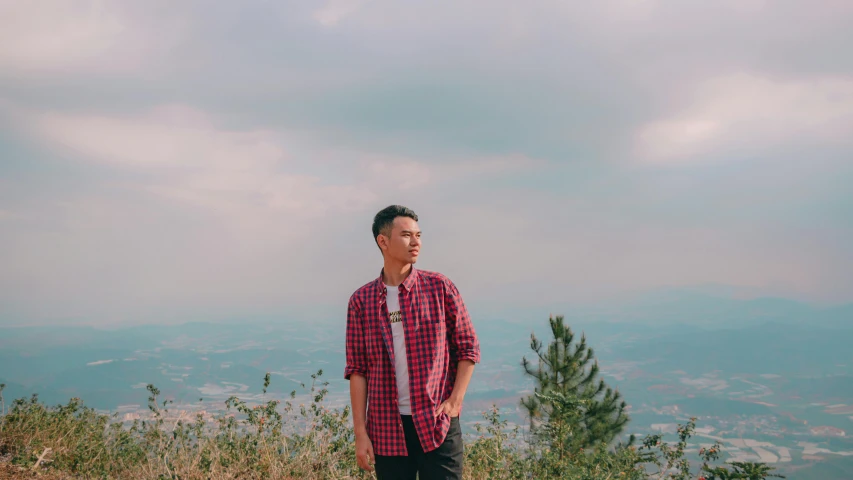 a man in plaid shirt looking over mountains from top of a hill