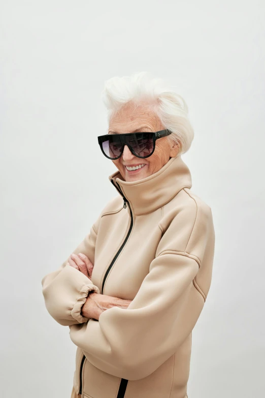 a woman in a beige coat with sunglasses and folded arms