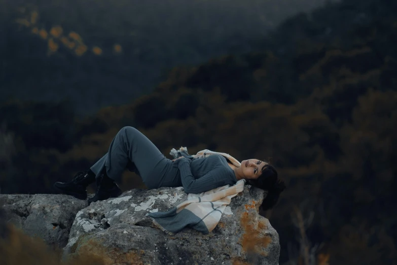 a beautiful woman laying on top of a rock with her head bowed