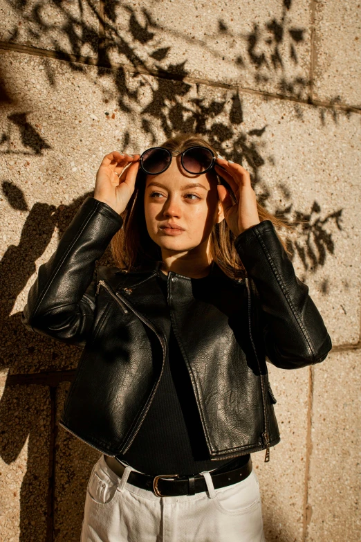 a woman with a leather jacket and glasses holding her hair