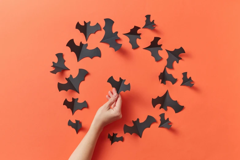 a hand arranging black bats in a circle against a bright orange background