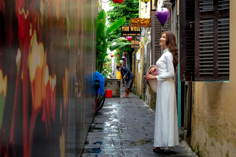 a woman wearing a long white dress standing in an alley way