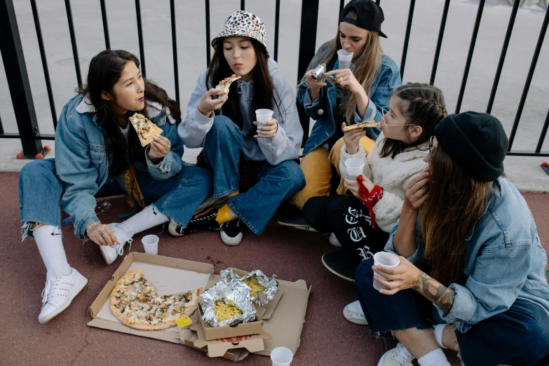 a group of girls sit eating food near a fence