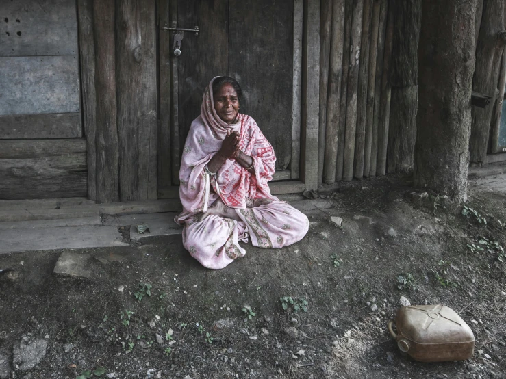 an older lady sitting on the ground by a wooden structure