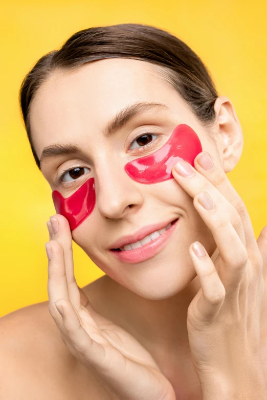 a woman with red eyeliner holding two red pieces of makeup over her face