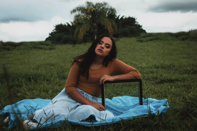 a woman sits on a blanket outside with a suitcase