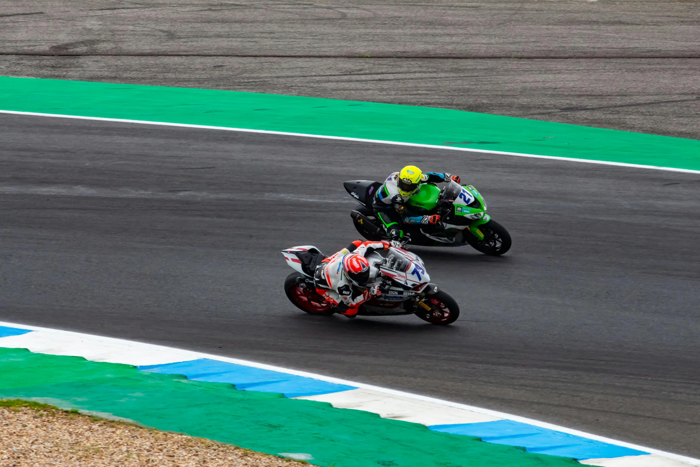 two people riding motorcycles around a track near grass