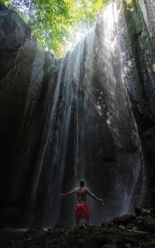 a man in red shorts standing in front of a waterfall