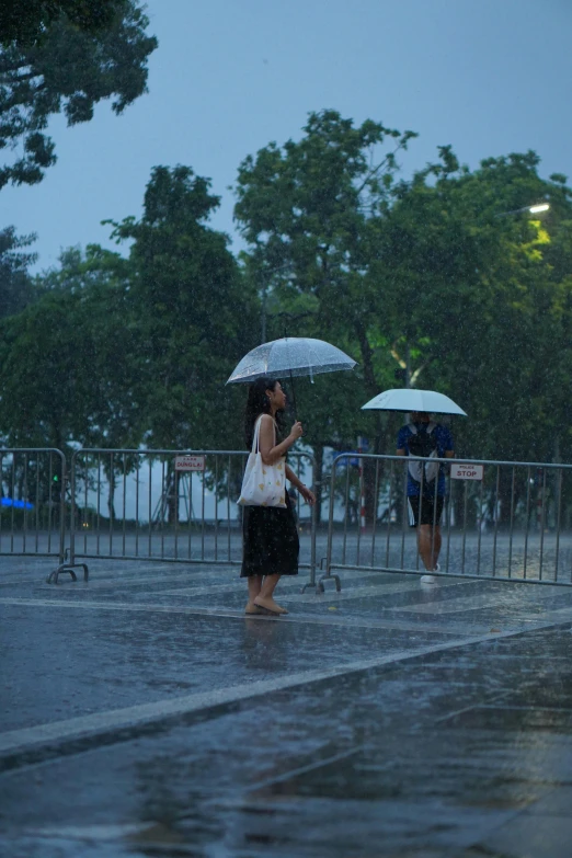 people standing in the rain with umbrellas near a fence