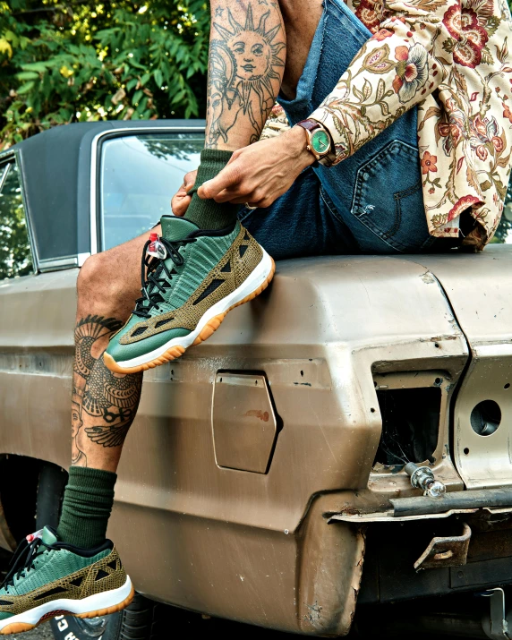 two people sit on the front fender of an old truck and are holding their feet up