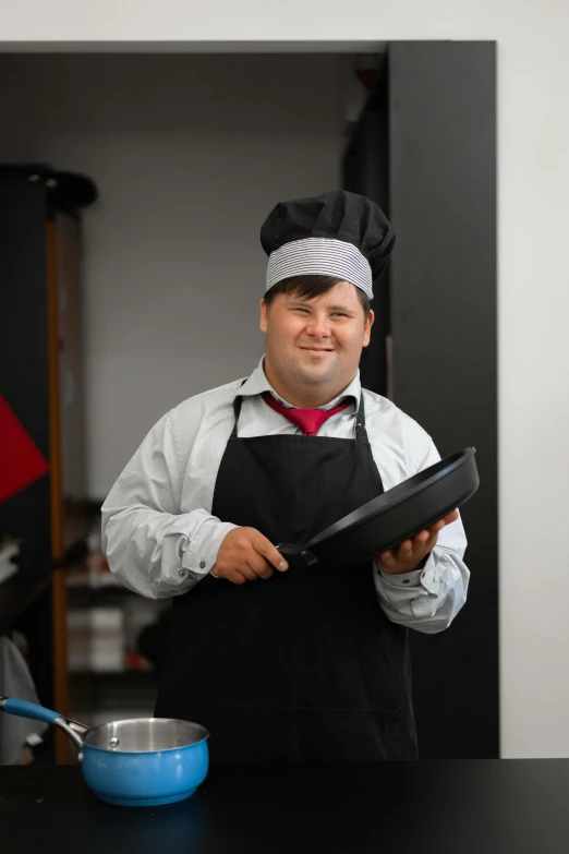 a man with an apron is holding a cooking pan and posing