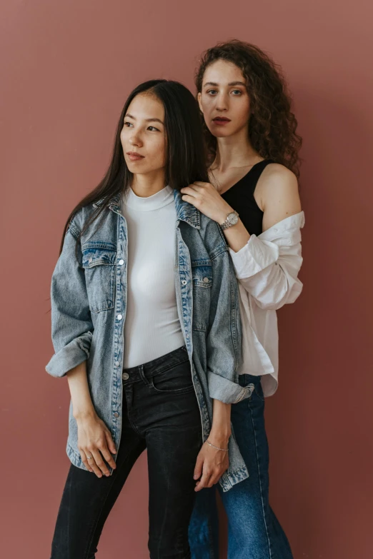 two women, one with a white shirt, are posing in front of a red wall