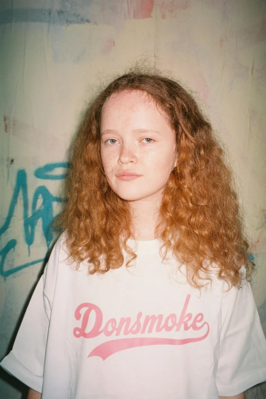 a young woman with long red hair wearing a t shirt and looking directly at the camera