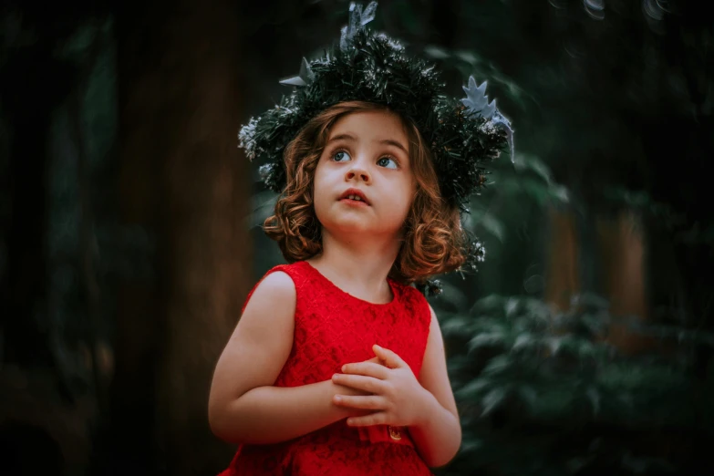 a little girl in a red dress with a crown on her head and hands up in front of her face