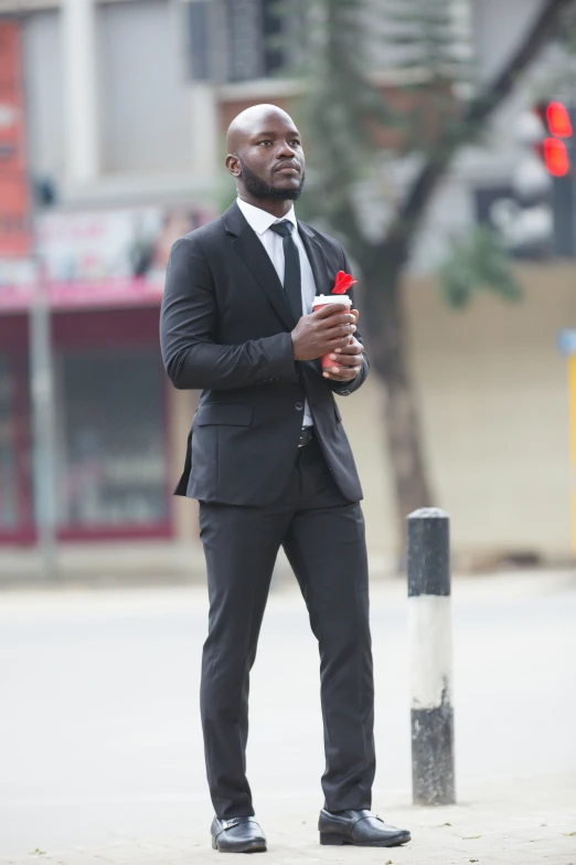 an african american man in a black suit is holding a red flower