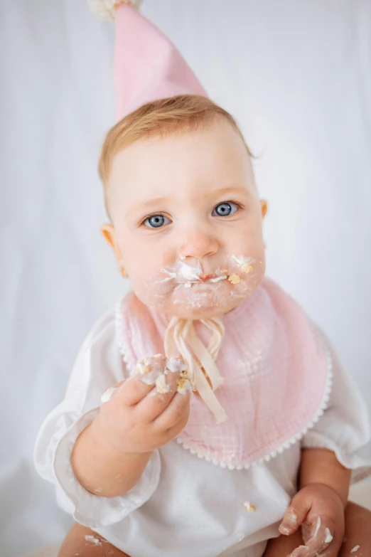 a little baby sitting down wearing a pink birthday hat and pacifier