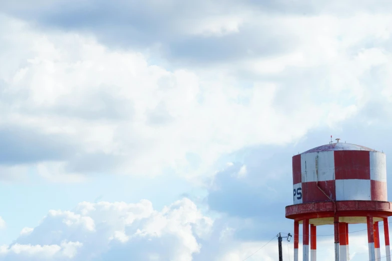 a tall red and white water tower with a sky background