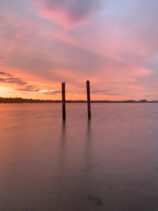 two wooden posts sticking out from the water in front of sunset