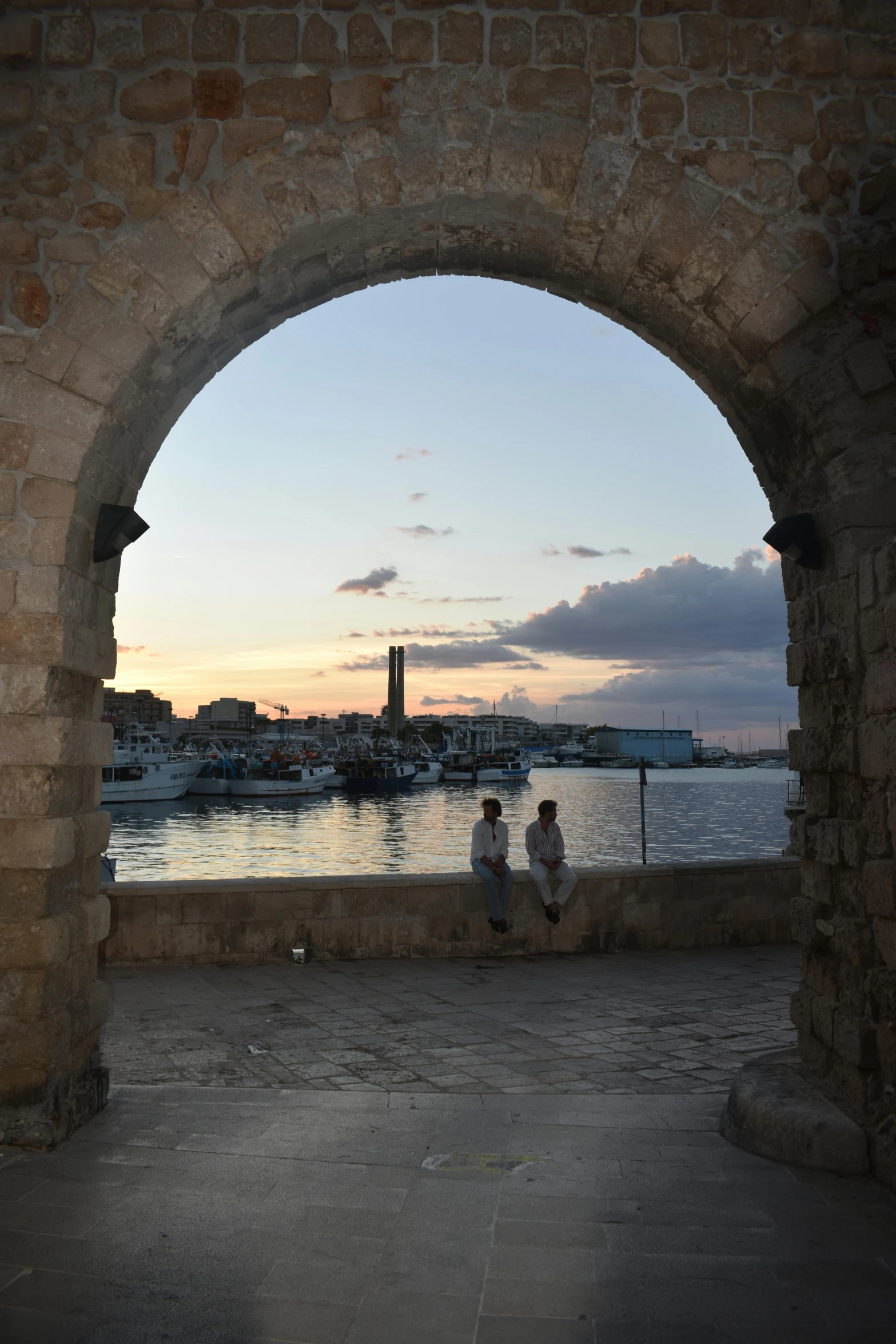 two people sitting under an archway looking out at the ocean