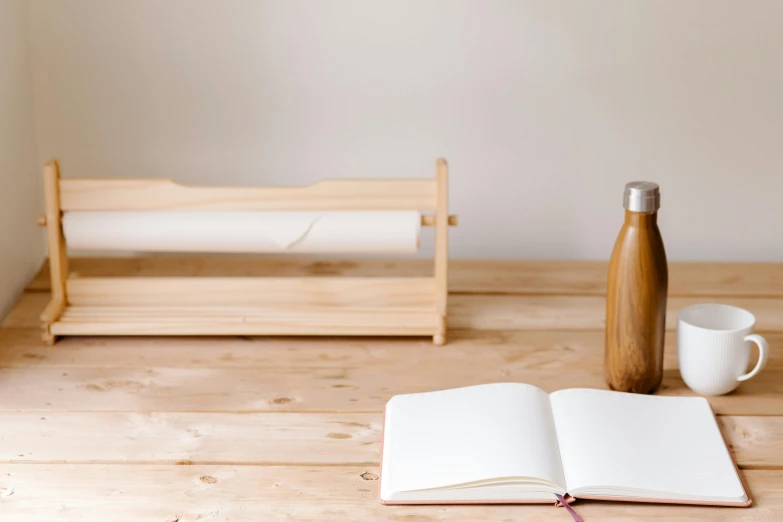 an open book sitting on top of a wooden table next to a cup and bottle