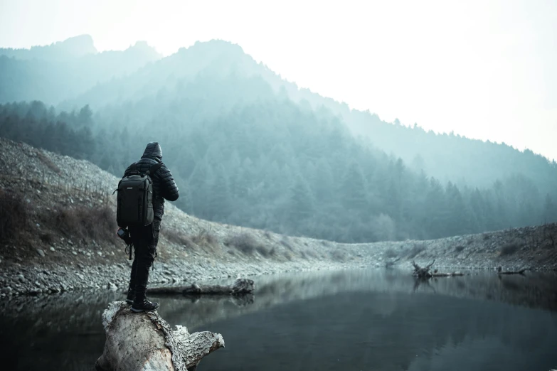 a man is standing on top of a log at the water's edge