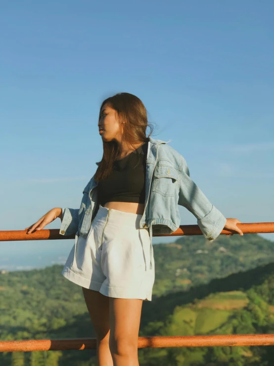 a woman is posing on the edge of a bridge overlooking the valley