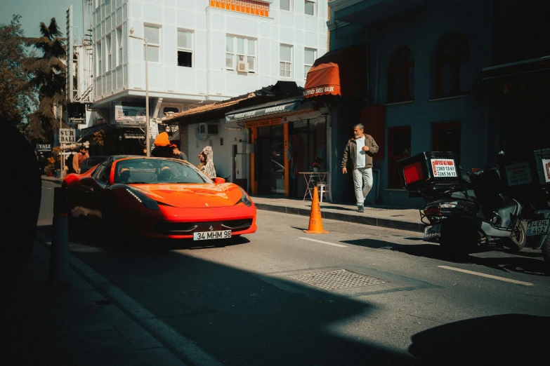 an orange sports car is parked near a traffic cone and people