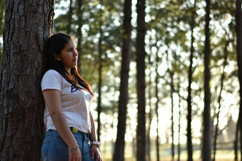 young woman leaning against a tree in a wooded area