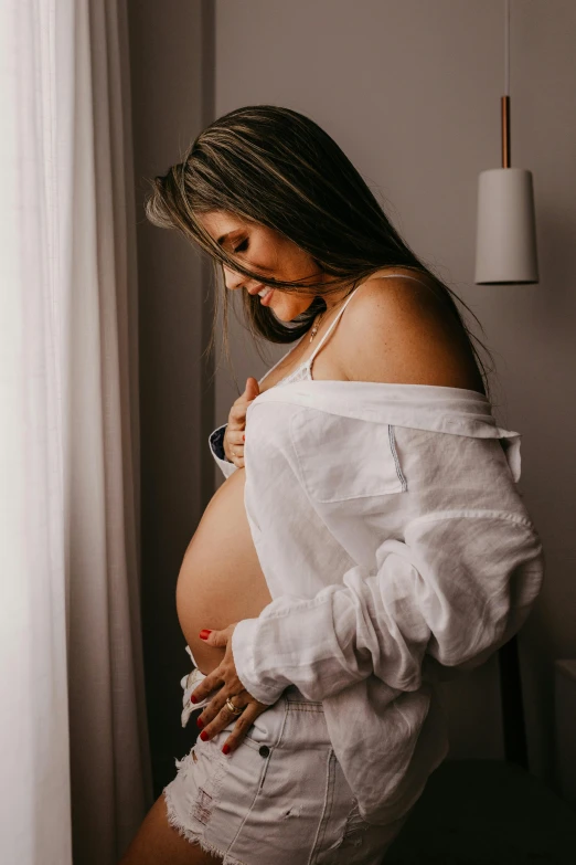 a pregnant woman in white shirt and ripped shorts posing for the camera